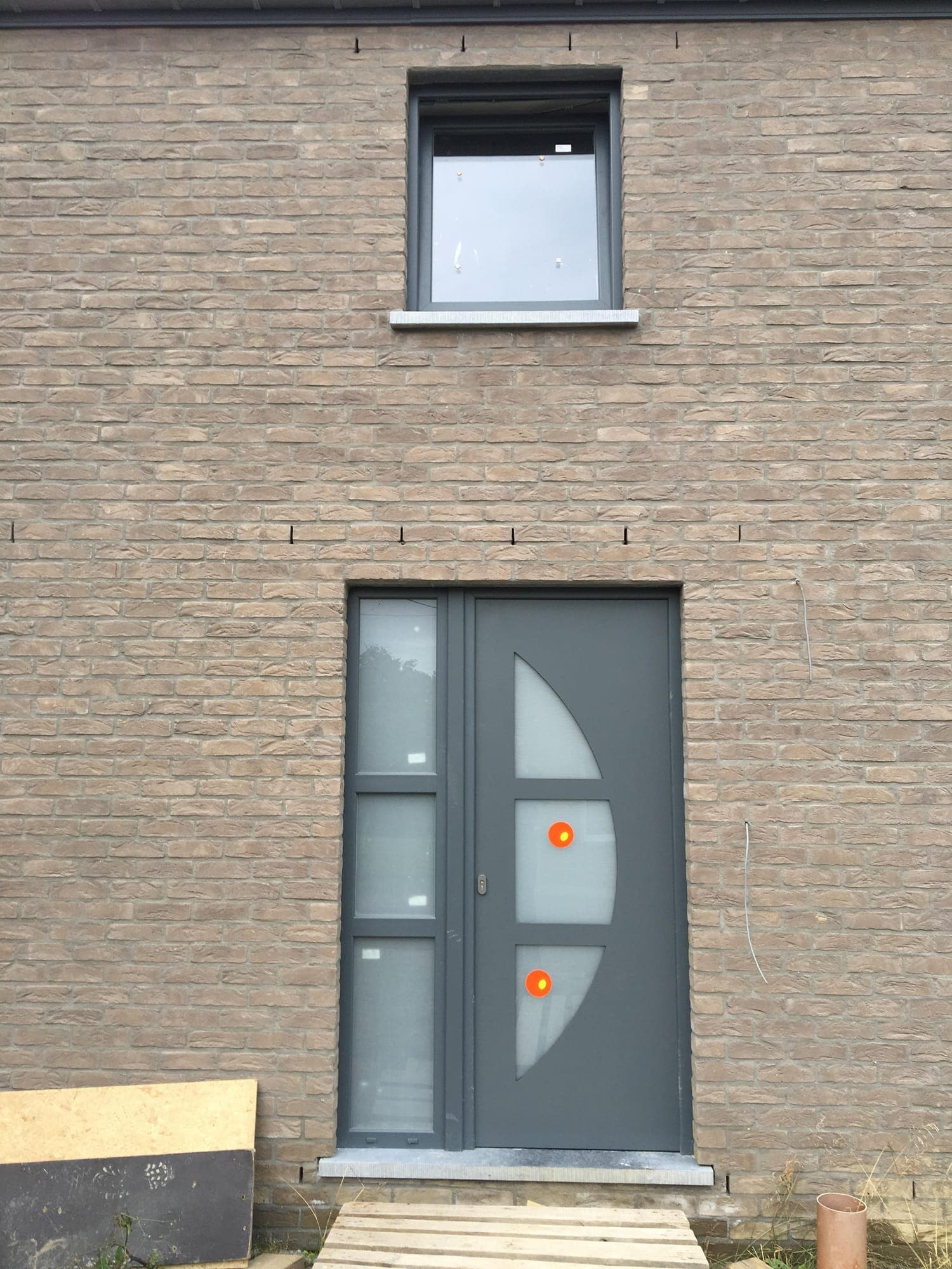 Porte d'entrée aluminium avec hublots vitrés sur façade brique